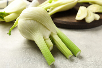 Whole and cut fennel bulb on light gray table, closeup