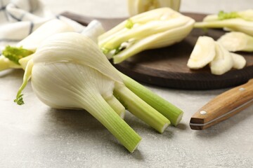 Whole and cut fennel bulb on light gray table, closeup