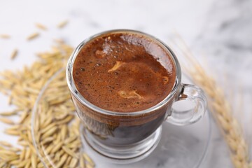 Cup of barley coffee, grains and spike on light table, closeup