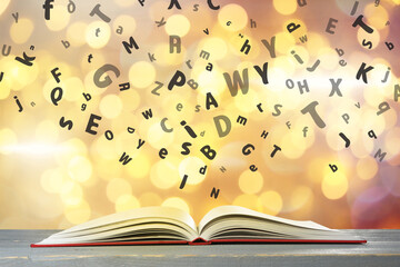 Letters flying out from open book on wooden table, bokeh effect