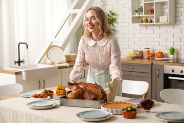 Beautiful young woman with tasty baked turkey at table in kitchen. Thanksgiving Day celebration
