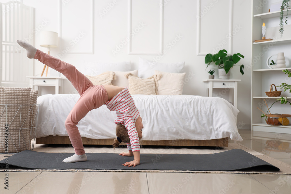 Poster cute little girl doing gymnastics on mat in bedroom