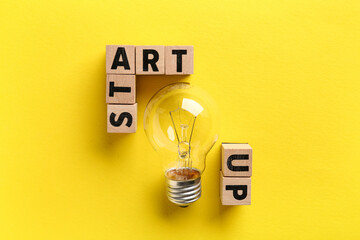 Cubes with word STARTUP and light bulb on yellow background