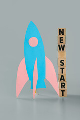 Cubes with text NEW START and paper rocket on grey background