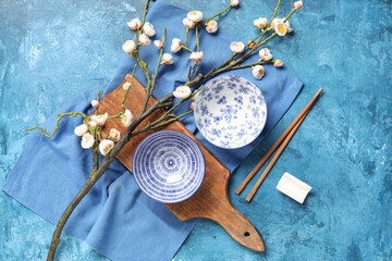 Wooden board with bowls, chopsticks and sakura branch on blue grunge background. Chinese table setting
