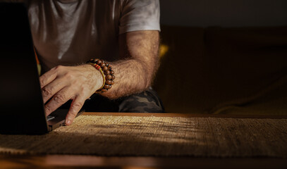 Closeup of arm of adult man using laptop with bracelets on wrist - obrazy, fototapety, plakaty