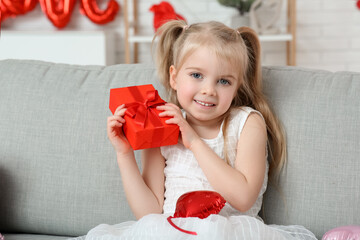 Cute little girl with gift box sitting in room decorated for Valentines Day