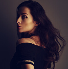 Beautiful makeup sensual woman with brown long hair and black dress looking on dark shadow...