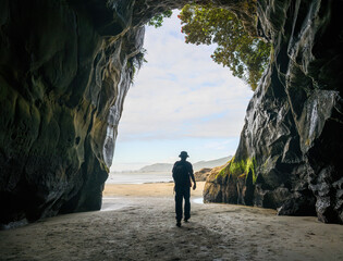 Entrance to Muriwai cave with a silhouette man walking. Muriwai Beach in summer. Auckland.