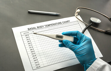 basal body temperature chart on the table and a gloved hand holding a thermometer