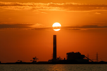 Sunset behind an industrial factory and in front is the sea, orange color, silhouette