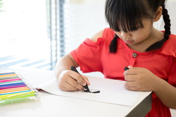 Asian little girl drawing with colorful pens on the table at home