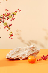 A stone slab and a tangerine are placed on the table with decorative flower branches. Shadows on pastel background. Space decorated for Tet holiday.