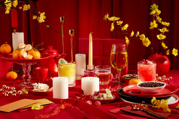 Front view of a brilliant banquet table with candles, wine, yellow apricot flowers and tangerines. Tet atmosphere with red background. Copy space-holiday theme.