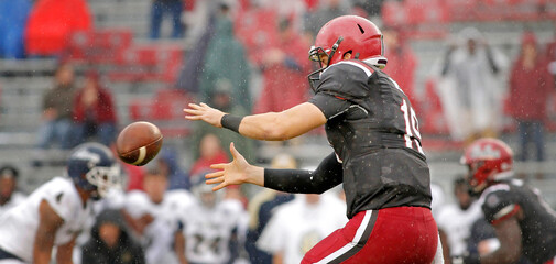 American football quarterback taking a snap in the rain while wearing helmet and pads. 