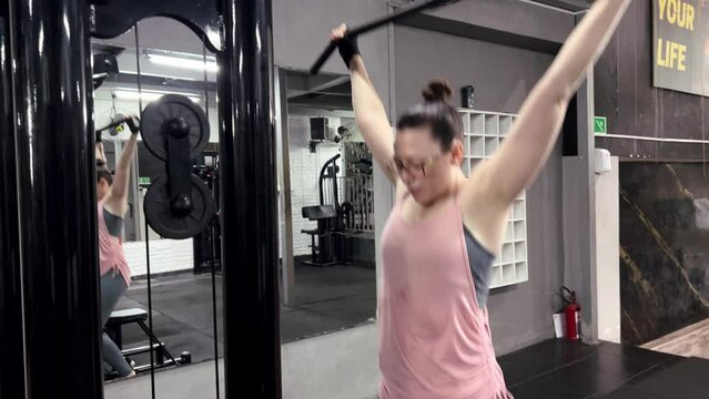 Woman with glasses exercising with a chin-up machine in the gym, exercise movements for arm muscles