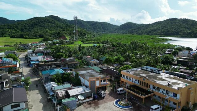 Aerial dolly of picturesque Filipino town center settlement with small buildings and satellite tower with lush mountains in background. Baras, Catanduanes.