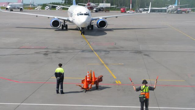 Jet airplane taxiing at airport, back view of aviation marshaller job at airport