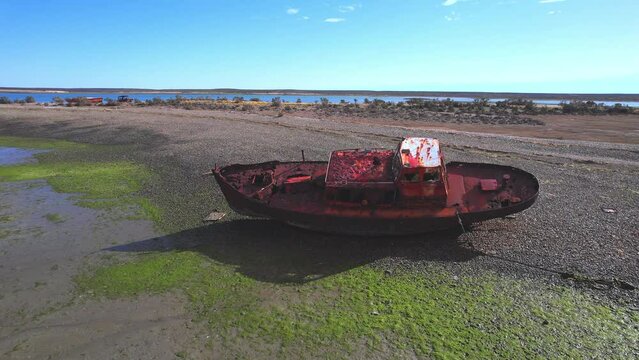 Circular Drone Shot of a Wrecked fishing boat which is rusted and lays on the beach at bahia  bustamante
