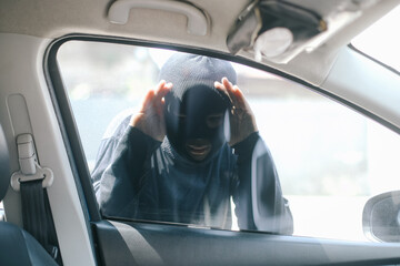 Man with balaclava on his head looking through car window and wondering how to break into the car....