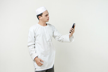  muslim man holding mobile phone and give stressful frustated expression. People religious Islam lifestyle concept. celebration Ramadan and ied Mubarak. on isolated backgroun.