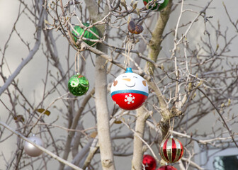 Snowman ornament with basic ball ornaments hanging from outdoor tree in autumn winter, branches bare.