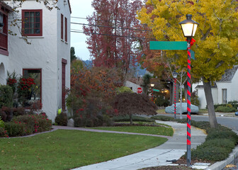 Old Fashioned Street Lights burning at sunset, covered in red ribbon and bow for Christmas. Street signs blank for your text. Sidewalk in residential neighborhood.