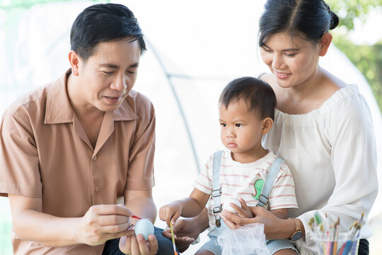 Asian family father, mother and little son painting eggs with brush in class workshop