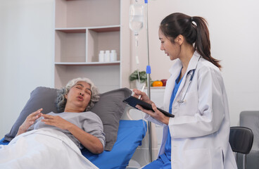 Obraz premium Elderly Asian woman lying in hospital bed looking unwell, with young Asian doctor take a history of illness Health check and encouragement.