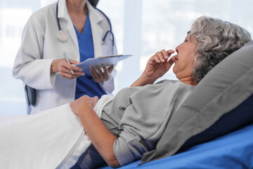 Fototapeta premium Elderly Asian woman lying in hospital bed looking unwell, with young Asian doctor take a history of illness Health check and encouragement.