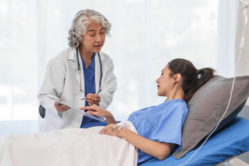 Obraz premium An elderly Asian doctor with a stethoscope is checking young Asian patient in hospital bed, take history of illness Health check and encouragement