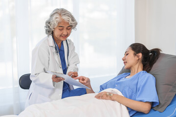 Obraz premium An elderly Asian doctor with a stethoscope is checking young Asian patient in hospital bed, take history of illness Health check and encouragement