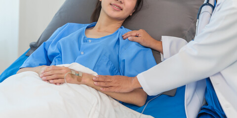 An elderly Asian doctor with a stethoscope is checking young Asian patient in hospital bed, take history of illness Health check and encouragement