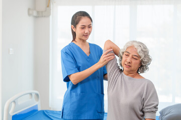 Fototapeta premium A young Asian nurse is assisting an elderly Asian woman with a grey hair during a physical therapy session.