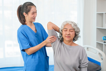 Fototapeta premium A young Asian nurse is assisting an elderly Asian woman with a grey hair during a physical therapy session.