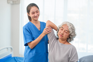 Fototapeta premium A young Asian nurse is assisting an elderly Asian woman with a grey hair during a physical therapy session.