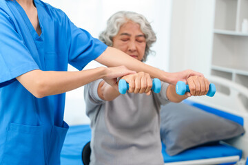 A young Asian nurse is assisting an elderly Asian woman with a grey hair during a physical therapy session.