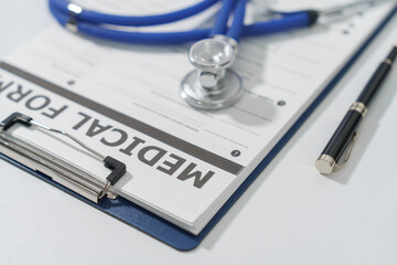 A blue stethoscope, clipboard with medical form, and a pen lie on a white surface, suggesting a clinical setting.