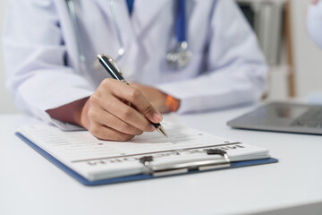 Medical doctor person hand is writing on a medical form on clipboard, on a white surface at medical...