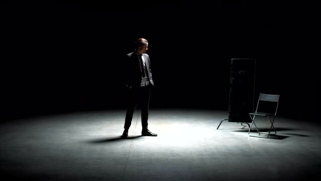 Man in suit alone on theater stage. Stock footage. Single attractive man in suit is playing on stage of theater. Man in suit with mirror is alone on dark theatrical stage