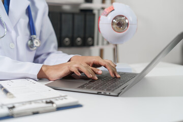 A doctor's hands are seen typing on a laptop keyboard with a stethoscope around the neck on white...