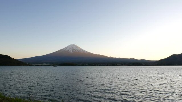 Mt Fuji peak lit by soft sunset light, Kawaguchiko shore in dusk, ripply water on foreground. Famous view of Fujisan across Lake Kawaguchi, shot at good autumn day evening
