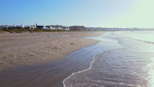 Drone pullback over wet sand and small waves rolling into beach, Paternoster