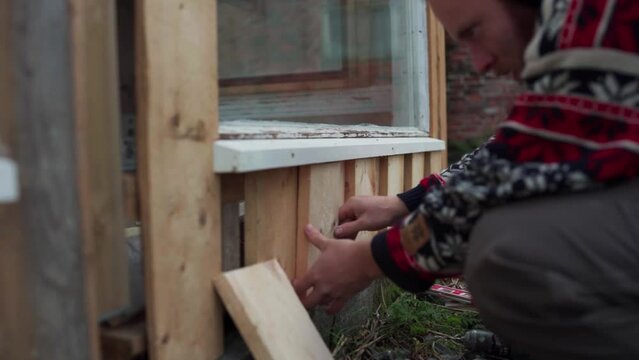 Man Installing Wood Planks On Doorway. Building DIY Greenhouse In Norway. timelapse