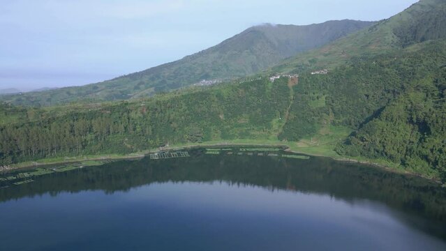 Aerial view of green lake among mountain cliffs and forest. Landscape Menjer Lake or "Telaga Menjer". 4K drone shot tropical lanke.