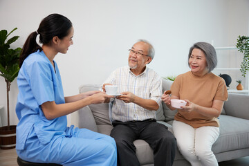 nurse or caregiver giving a cup of tea and coffee to senior couple at home