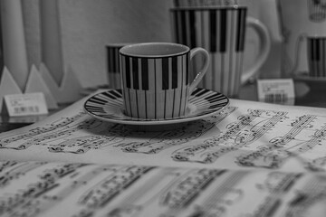 Eine Tasse mit Klaviertasten stehend auf  einem Notenblatt, A cup with piano keys standing on a sheet of music, Tasse auf Notenblatt - obrazy, fototapety, plakaty
