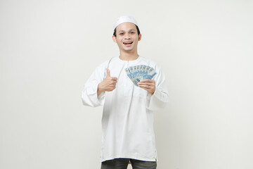 happy muslim man holding money rupiah banknotes and  give thumb up. People religious Islam lifestyle concept. celebration Ramadan and ied Mubarak. on isolated background.