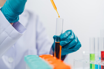 A scientist examines samples with a microscope in a laboratory with test tubes filled with colorful...