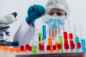 A scientist examines samples with a microscope in a laboratory with test tubes filled with colorful...